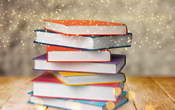 A stack of books on a wood table with gold dust falling from the top